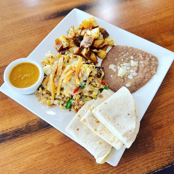 A breakfast plate with scrambled eggs, roasted potatoes, refried beans, tortillas, and a side of salsa.