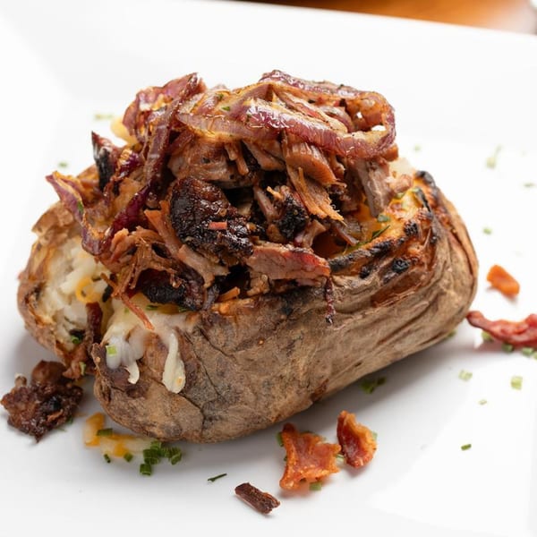 A Harold Dean Smoked Goods baked potato, topped with pulled pork, caramelized onions, and melted cheese.