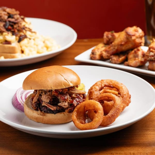 Harold Dean's pulled pork sandwich with red onion and onion rings, with other BBQ dishes in the background.