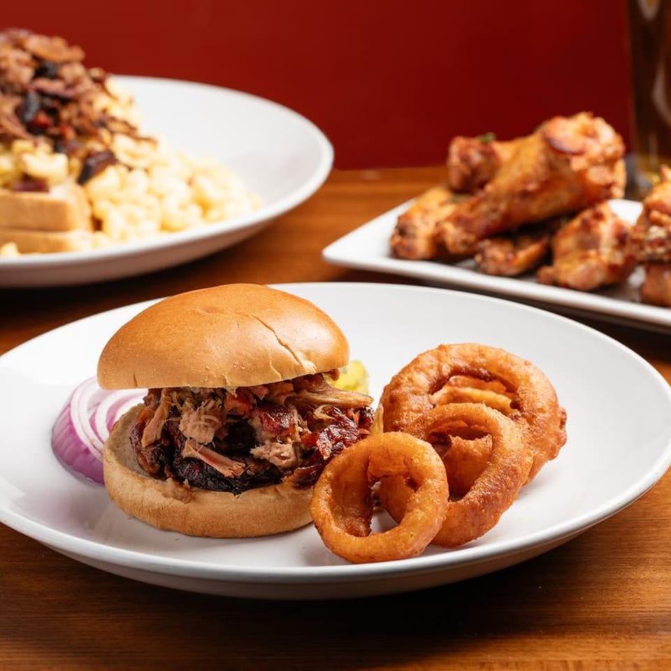 Harold Dean's pulled pork sandwich with red onion and onion rings, with other BBQ dishes in the background.