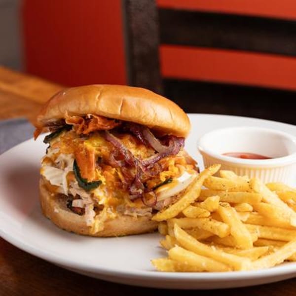 Harold Dean's pulled pork sandwich with caramelized onions and fries on a white plate.