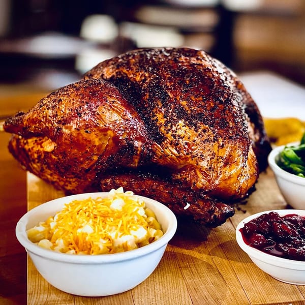 A whole smoked turkey with sides of macaroni and cheese, green beans, and cranberry sauce.